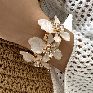 Dettaglio del bracciale dorato con tre fiori in smalto bianco a strati indossato al polso