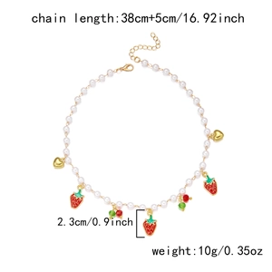Détail du collier de perles avec pendentifs fraise et coeur doré sur fond blanc