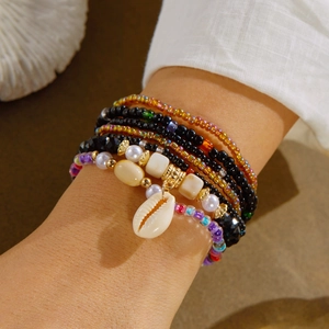 Detail of layered bohemian beaded bracelets with white shell charm on female wrist