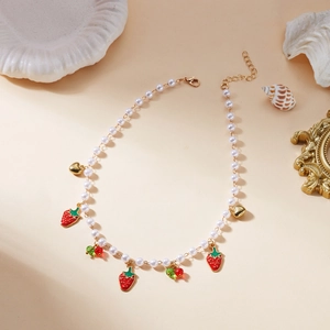 Détail du collier de perles avec breloques fraises et cœurs sur décor vintage