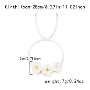 Detail eines geflochtenen Armbands mit weißen Plumeria-Blüten und funkelnden Strasssteinen