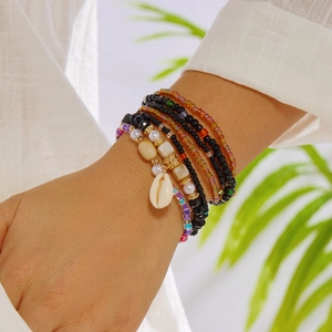 Detail of bohemian layered colorful bead bracelets with natural seashell charm on model