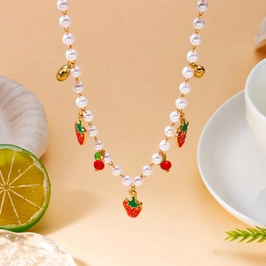 Détail du collier de perles avec breloques fraises rouges et cloches dorées sur fond beige