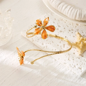 Détail d'un bracelet de bras torsadé doré avec fleurs en émail orange et finitions polies