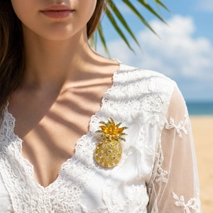 Close-up of a luxury crystal pineapple brooch pinned on white lace dress in sunlit beach setting