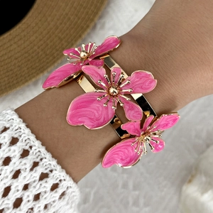 Primo piano del bracciale dorato con fiori in smalto rosa su una manica di pizzo