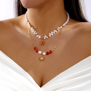 Gros plan du collier double rang avec perles baroques, pendentifs soleil et perles rouges