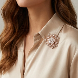 Détail d'une broche flocon en or rose avec perles portée sur une chemise en soie
