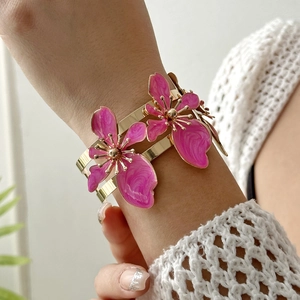 Dettaglio ravvicinato di un largo bracciale dorato con due fiori in smalto rosa e oro