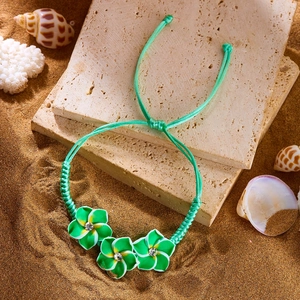 Detail eines grünen gewebten Frangipani-Armbands mit Muschel und Koralle am Strand
