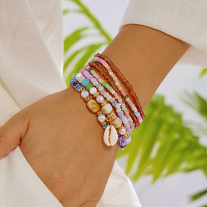 Detail of bohemian layered colorful bead bracelets with a white shell charm for beach style