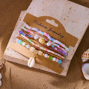 Detail view of Bohemian multi-layer beaded bracelets with a seashell charm on sand
