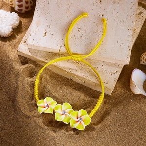 Detailaufnahme eines handgefertigten gelben Webarmbands mit gelben Frangipani-Blüten am Strand