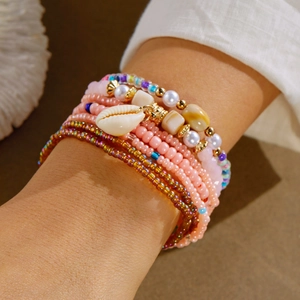 Detail of bohemian layered colorful bead bracelets featuring a white shell charm and pearls