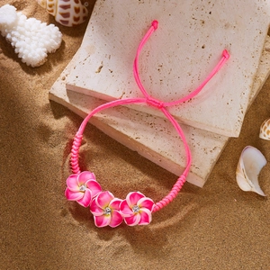 Nahaufnahme eines rosa Flechtarmbands mit Plumeria-Blüten und Strass auf feinem Sand