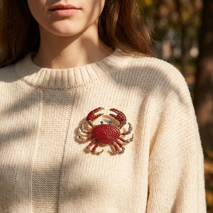 Sparkling crab brooch with red rhinestones pinned on a beige knitted sweater fabric