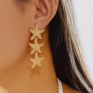 Close-up of triple starfish drop earrings in gold finish worn by a female model