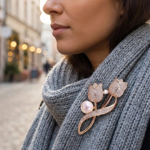Gros plan d'une broche tulipe en or rose avec strass brillants et perle rose sur une écharpe