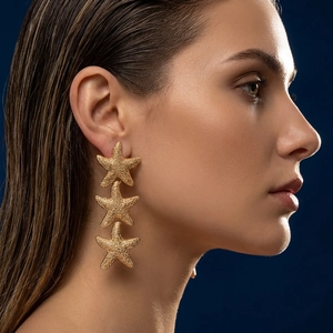 Detail view of triple golden starfish dangle earrings with matte texture on female model