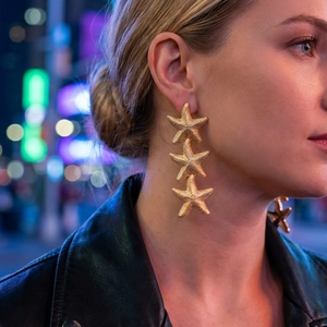 Close-up of golden triple starfish drop earrings with a matte textured finish on a model