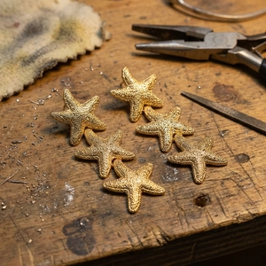 Detail of six golden starfish earrings with grainy texture on a vintage wooden workbench