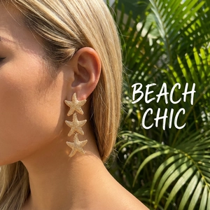 Close-up of golden triple starfish drop earrings with textured finish worn on ear