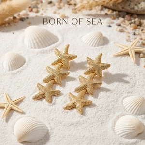 Detailed view of gold starfish drop earrings on white sand beach with coastal shells