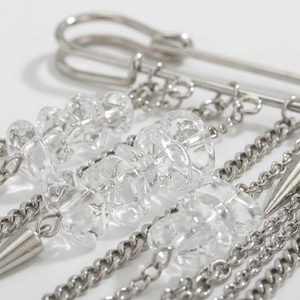Detail of silver safety pin brooch with hanging chains, textured beads and metal spikes