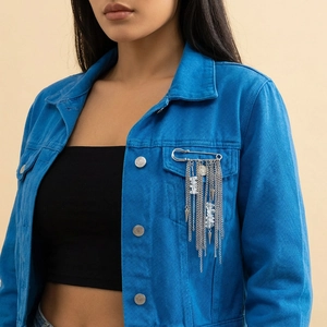 Close-up of silver punk brooch with tassels and beads on a blue denim jacket