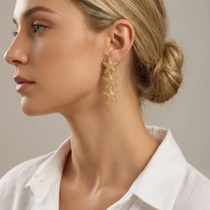 Macro shot of gold-tone triple starfish drop earrings with matte sandblasted texture