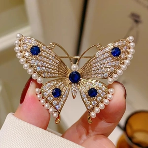 Golden butterfly brooch with white pearls, dense crystals, and blue gemstone accents