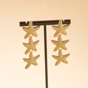 Macro detail of gold starfish drop earrings showing intricate textured surface on metal