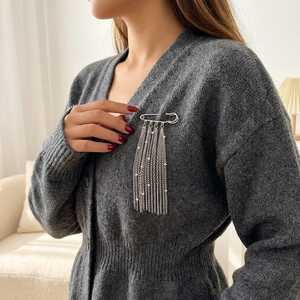 Detail of silver safety pin brooch with long chain tassels and pearls on gray knitwear