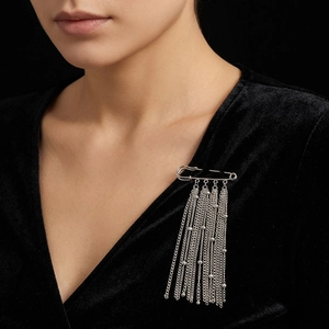 Detail of silver safety pin brooch with long metal fringe tassels on black velvet clothing