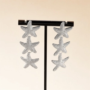 Macro shot of silver starfish drop earrings with three tiered ocean charms and textures