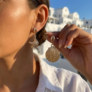 Detalle de pendientes de estrella de mar y concha dorados con cristales