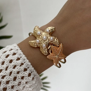 Detailed shot of a golden starfish cuff bracelet featuring white pearls on a female wrist