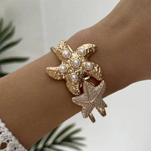 Detail of a golden starfish cuff bracelet featuring white pearls and elegant sea motifs