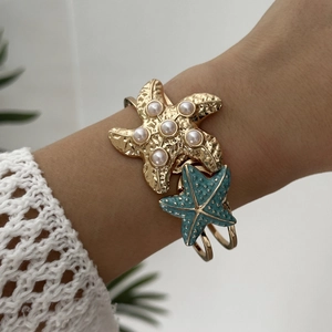 Detail of a gold starfish cuff featuring hammered metal textures and colorful enamel accents