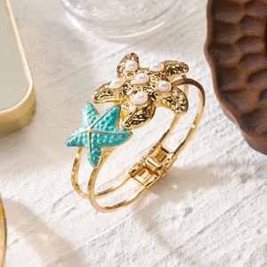 Detail of golden starfish bracelet with pearls and blue enamel on a sandy texture background