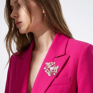 Detailed view of an elegant gold butterfly brooch with pearl on a vibrant pink blazer