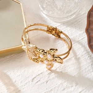 Detailed close-up of golden starfish bracelet with pearls on a textured summer background