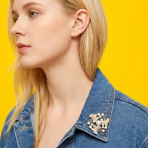 Detailed view of a golden butterfly brooch with pearls on a blue denim jacket collar