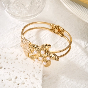 Detail of golden starfish bracelet with white pearls and cream enamel on double metal bands