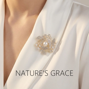 Macro detail of golden butterfly brooch with white pearl and sparkling crystals on silk shirt