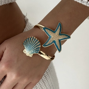 Detail of gold open cuff bracelet featuring blue starfish and shell beach motifs