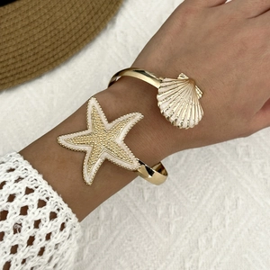 Detail of a gold ocean-themed cuff bracelet with starfish and shell on a beach hat background