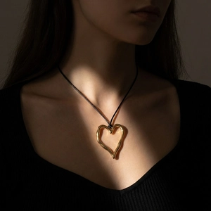 Detail of artistic gold heart pendant with irregular lava texture on black cord necklace