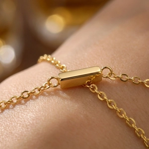 Macro di un ciondolo rettangolare in oro lucido su un bracciale a catena sottile e minimalista