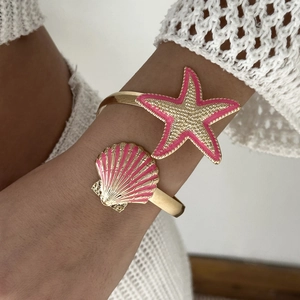 Close-up of golden starfish and shell cuff bracelet with pink enamel on female wrist